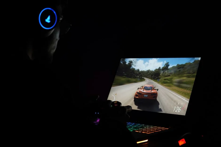 gamer using a laptop and headphones to play a racing game in a dark room